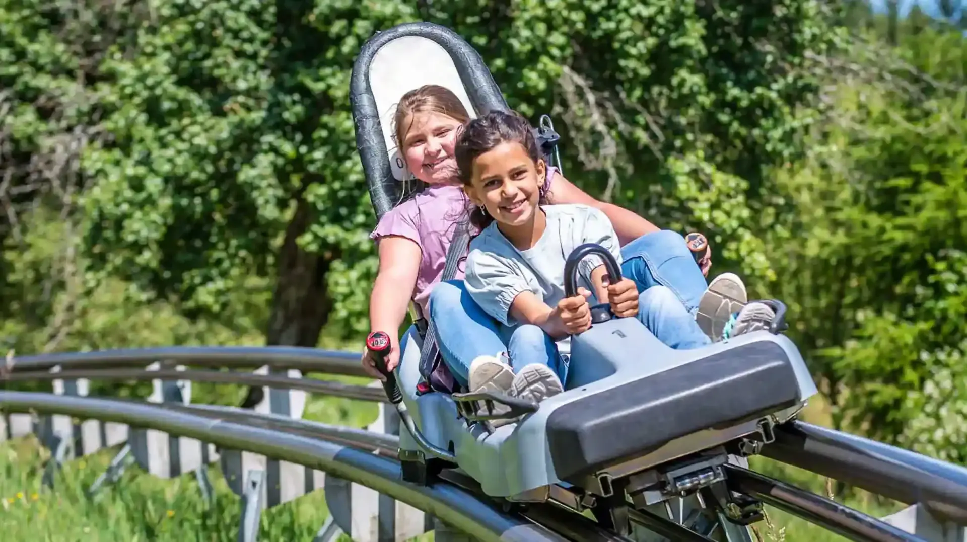 Personen fahren die Sommerrodelbahn Gutach hinab, umgeben von waldigen Bergen.